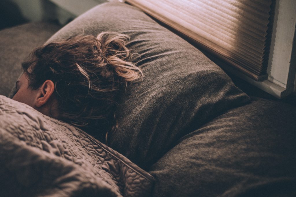 Eine Frau liegt schlafend im Bett, eingekuschelt in ihrer braunen Bettdecke.